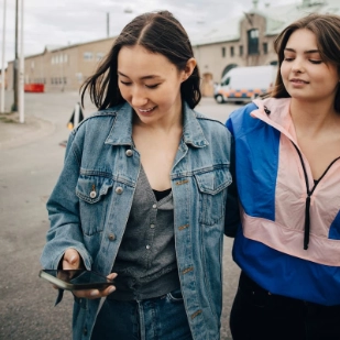 deux adolescentes marchent dans la rue, l'une d'elle regarde son smartphone